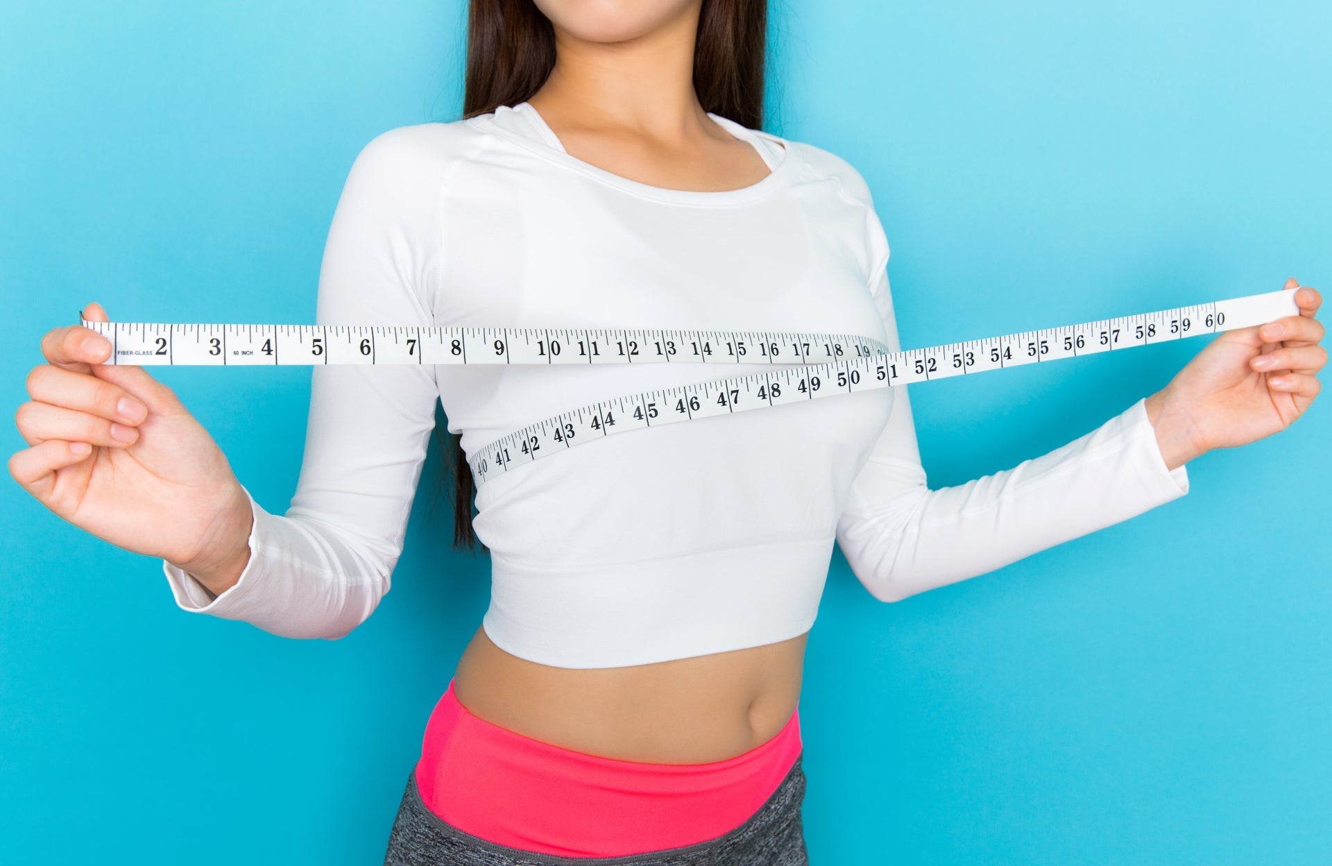 Woman in white tape with a measuring top around her chest, assessing her bra size for a perfect wardrobe solution