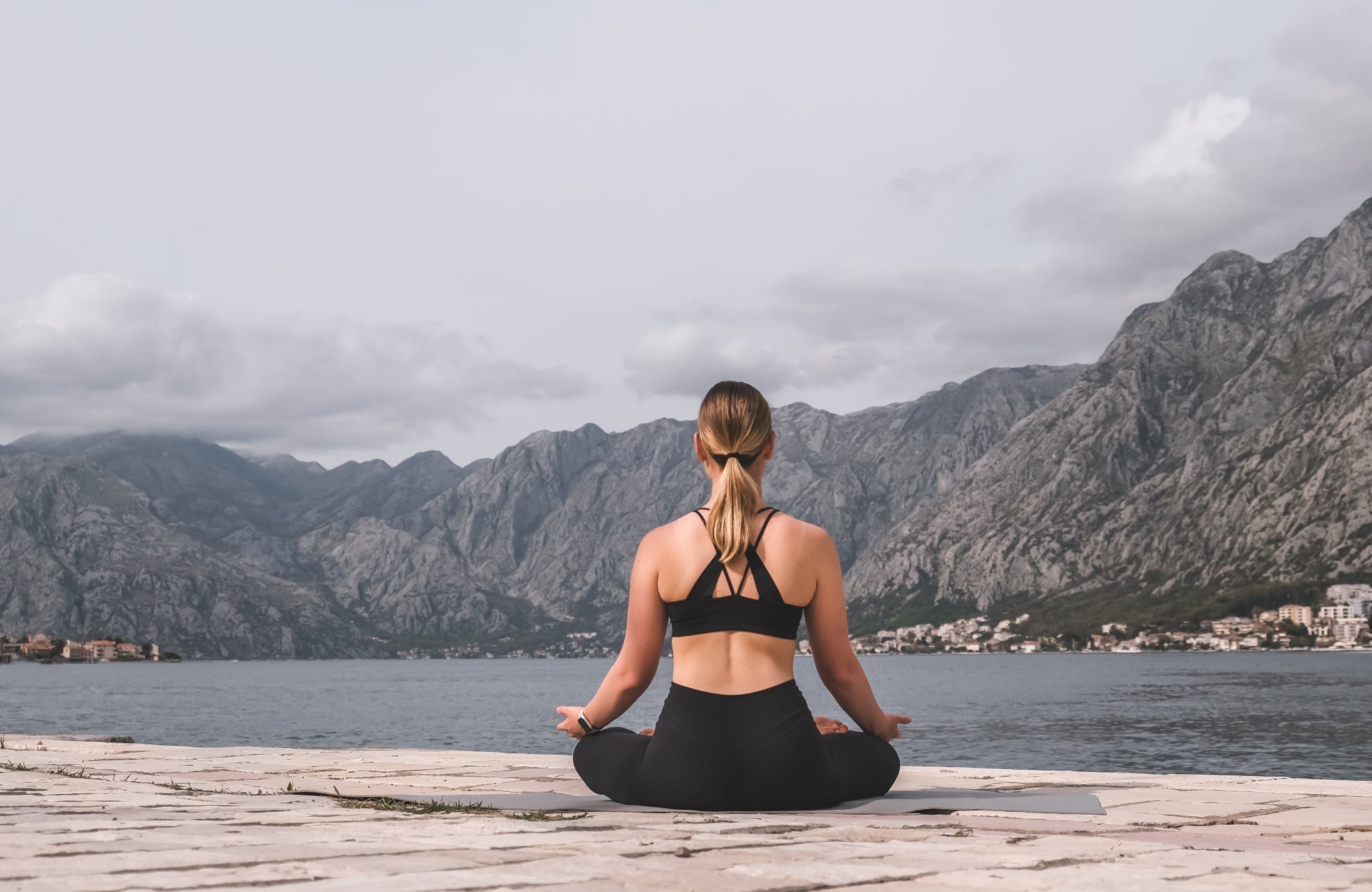 Woman meditating by a lake with mountains in the background