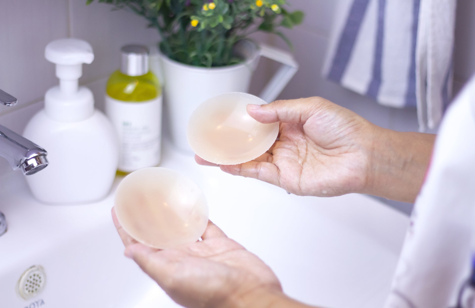 Woman washing silicone nipple covers over a sink with mild soap for maximizing their reusability and enhancing the lifespan of them